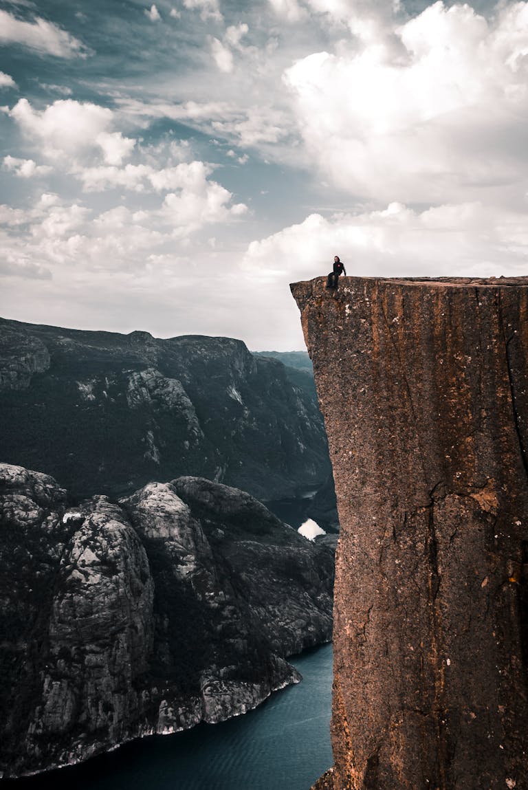 A daring traveler sits on the edge of Preikestolen, overlooking breathtaking Norwegian fjords.