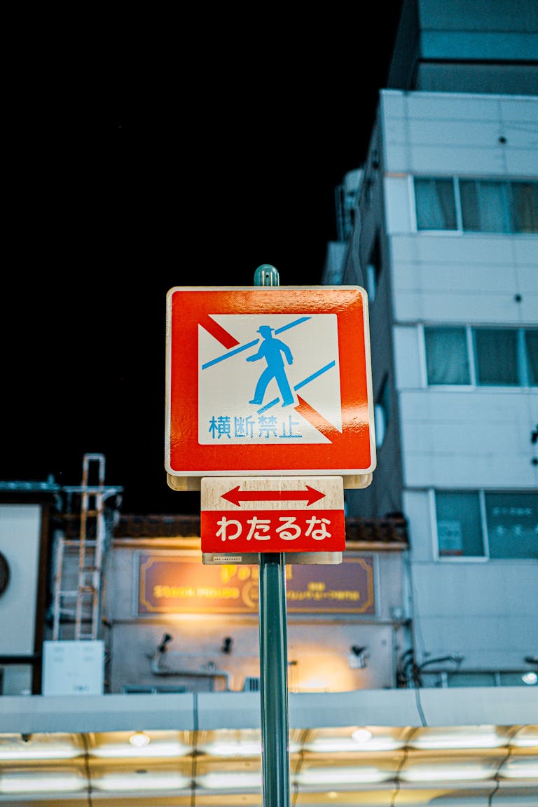 A Japanese prohibition sign in front of a building at night in an urban setting.