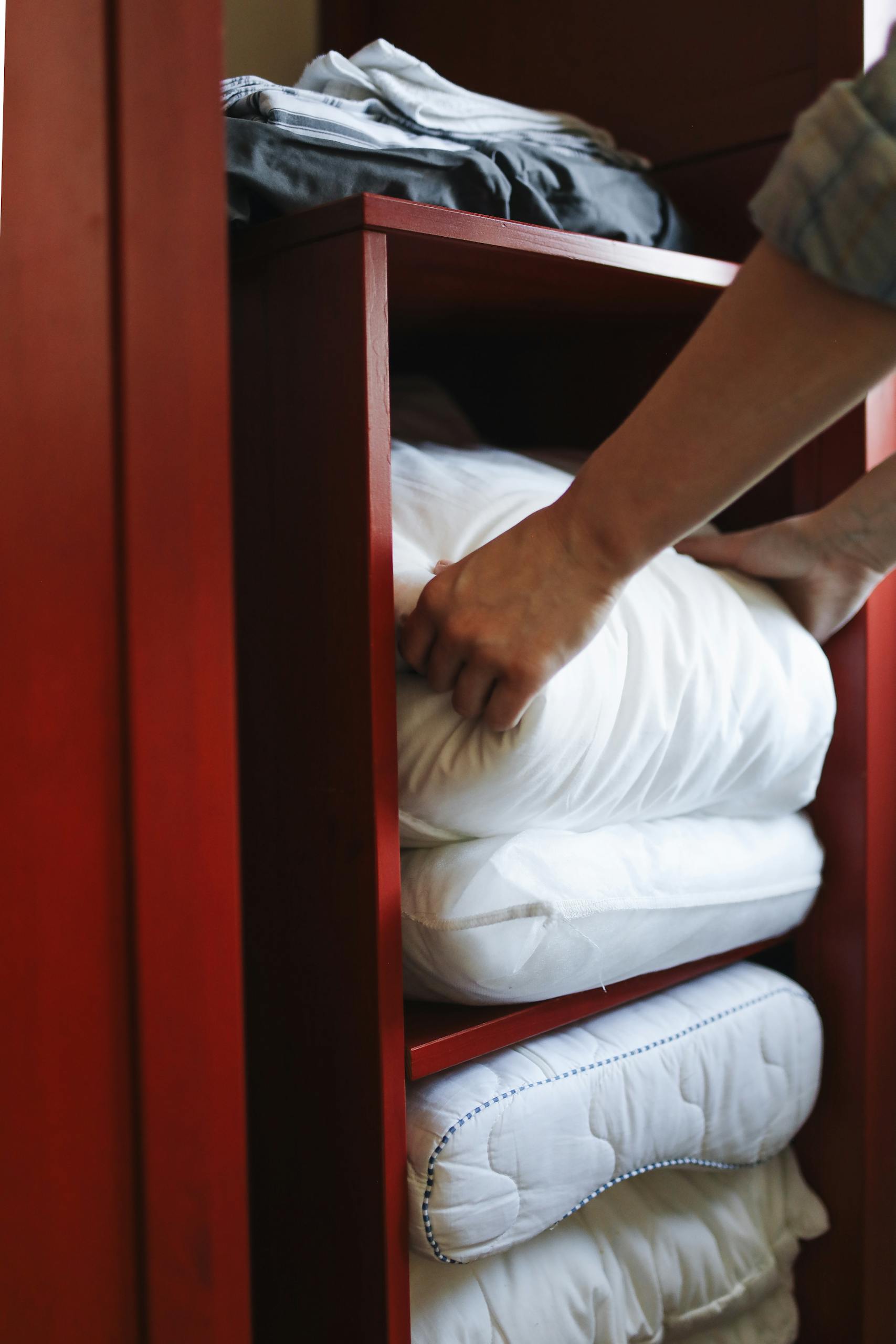 Hands organizing neatly folded linens in a red wooden cabinet.